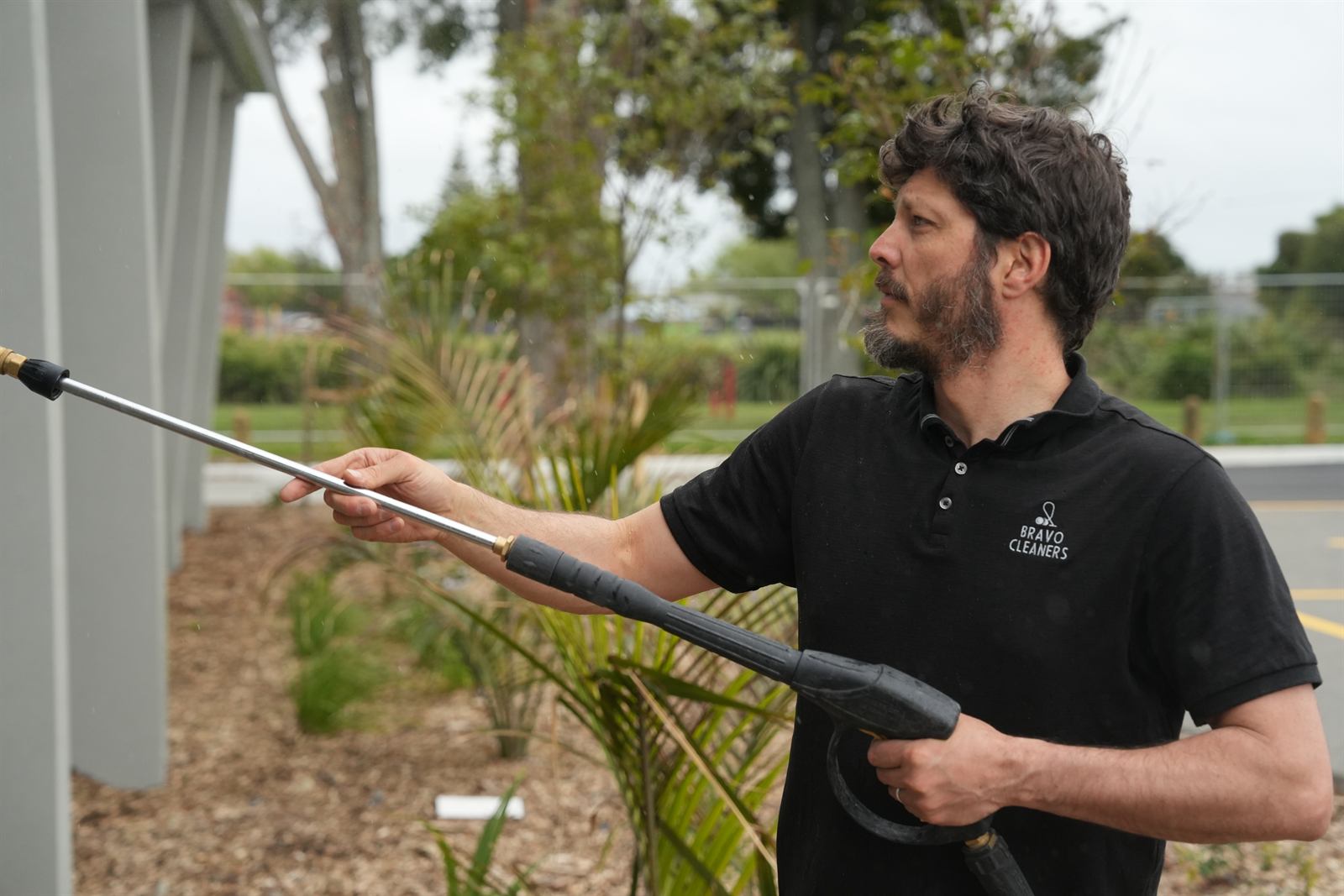 Bravo Cleaners team member soft-washing a building exterior with palm trees in the foreground