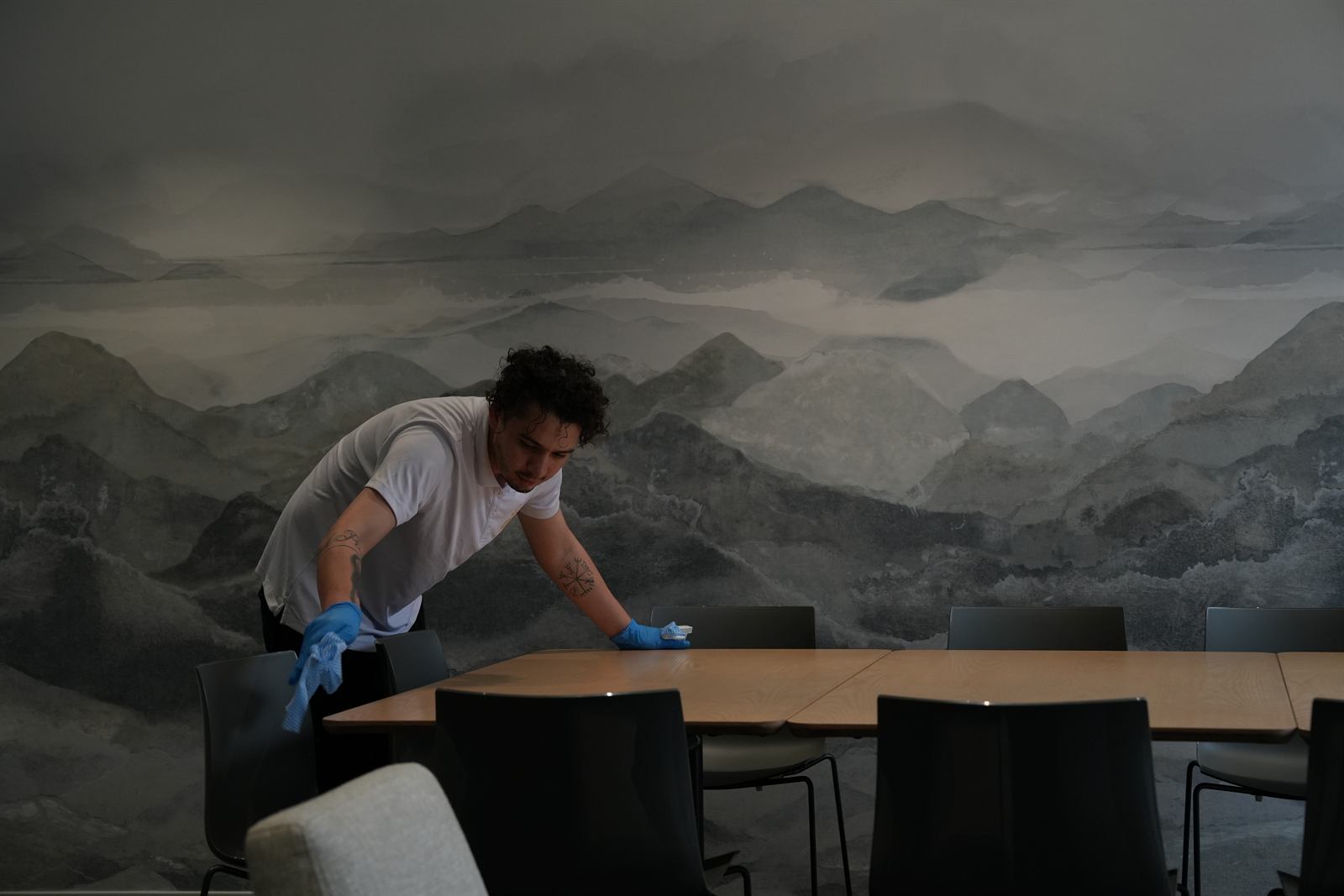 A Bravo Cleaners team member wiping down a corporate boardroom table with a mountain mural backdrop